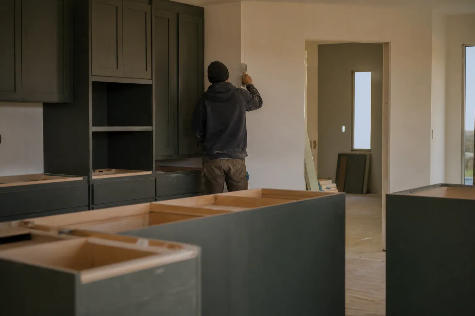 Commercial custom cabinets — a tradesperson seen from behind smoothing a long wall seam