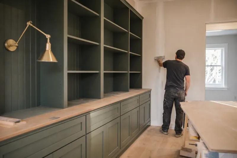 Custom office cabinets — a tradesperson seen from behind smoothing a long wall seam